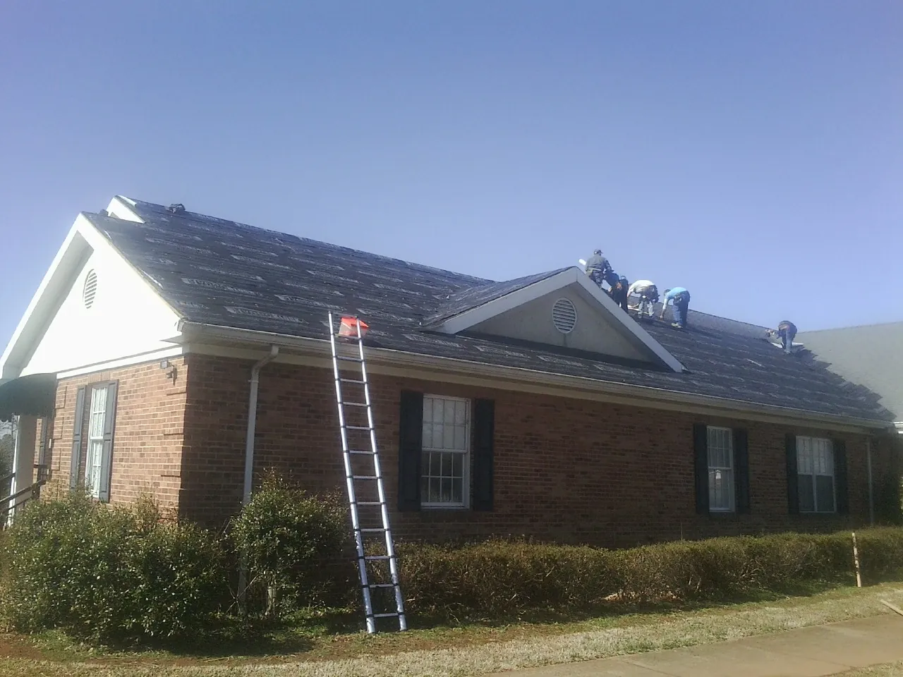 Crew tearing shingles off a brick ranch roof with a ladder set — Emergency Roof Repair work by our crew in Manteno