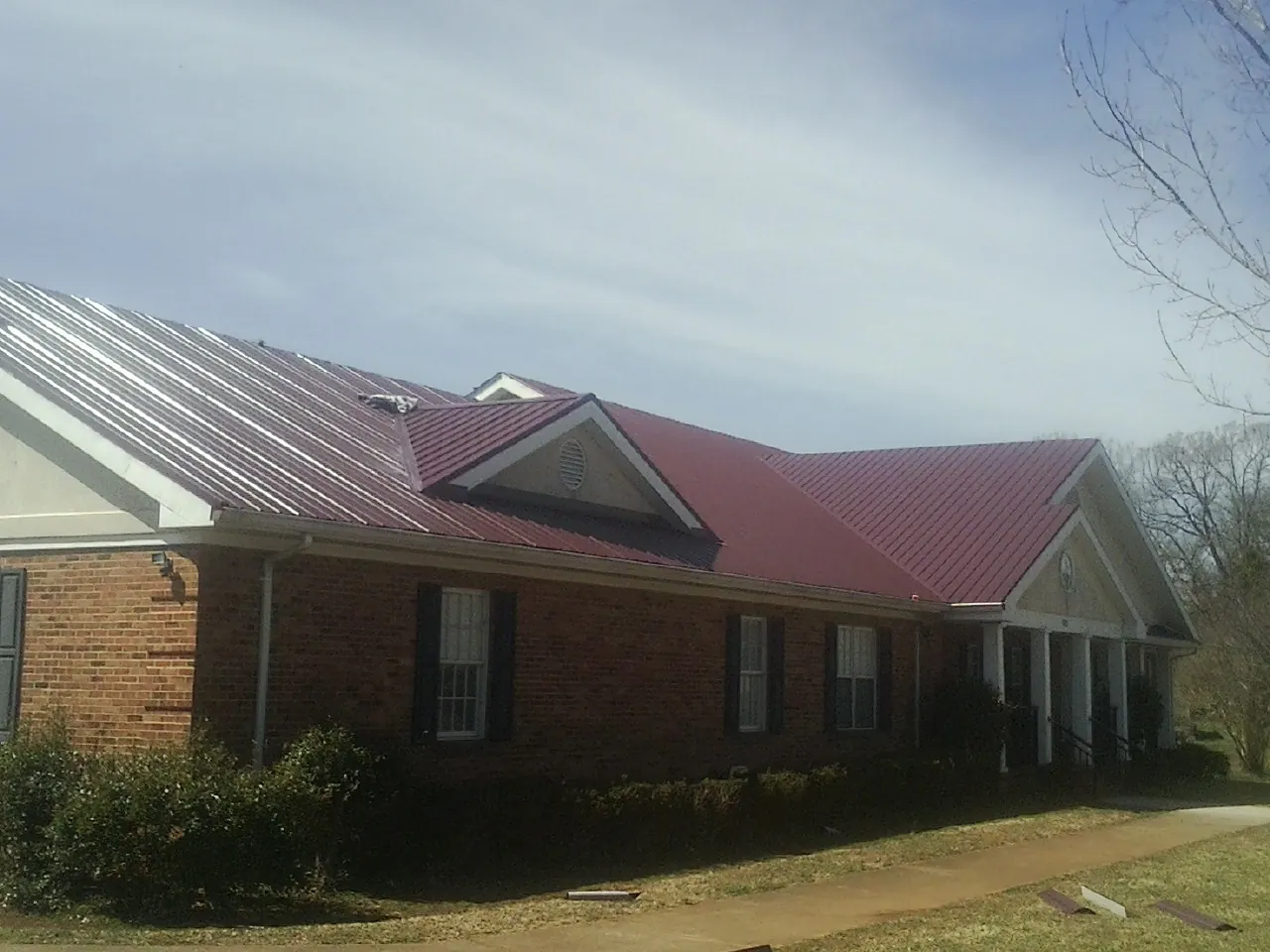 Red metal roof with gabled entries on a long brick building, from a Hail Damage Roof Repair job in Manteno