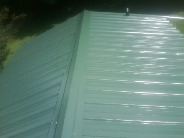 New green metal panels meeting at the ridge of a roof — Flat Roof Repair work by our crew in Manteno