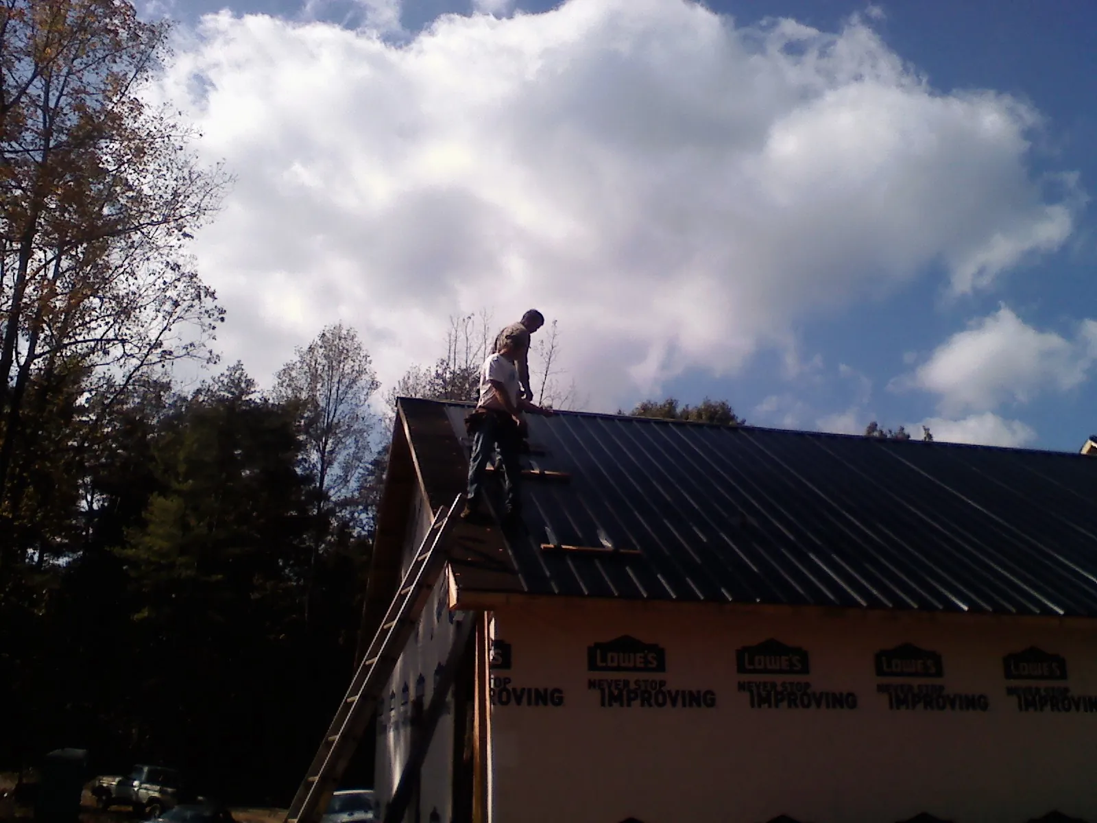 Roofer fastening dark metal panels high against a cloudy sky, from a Roof Inspection job in Manteno
