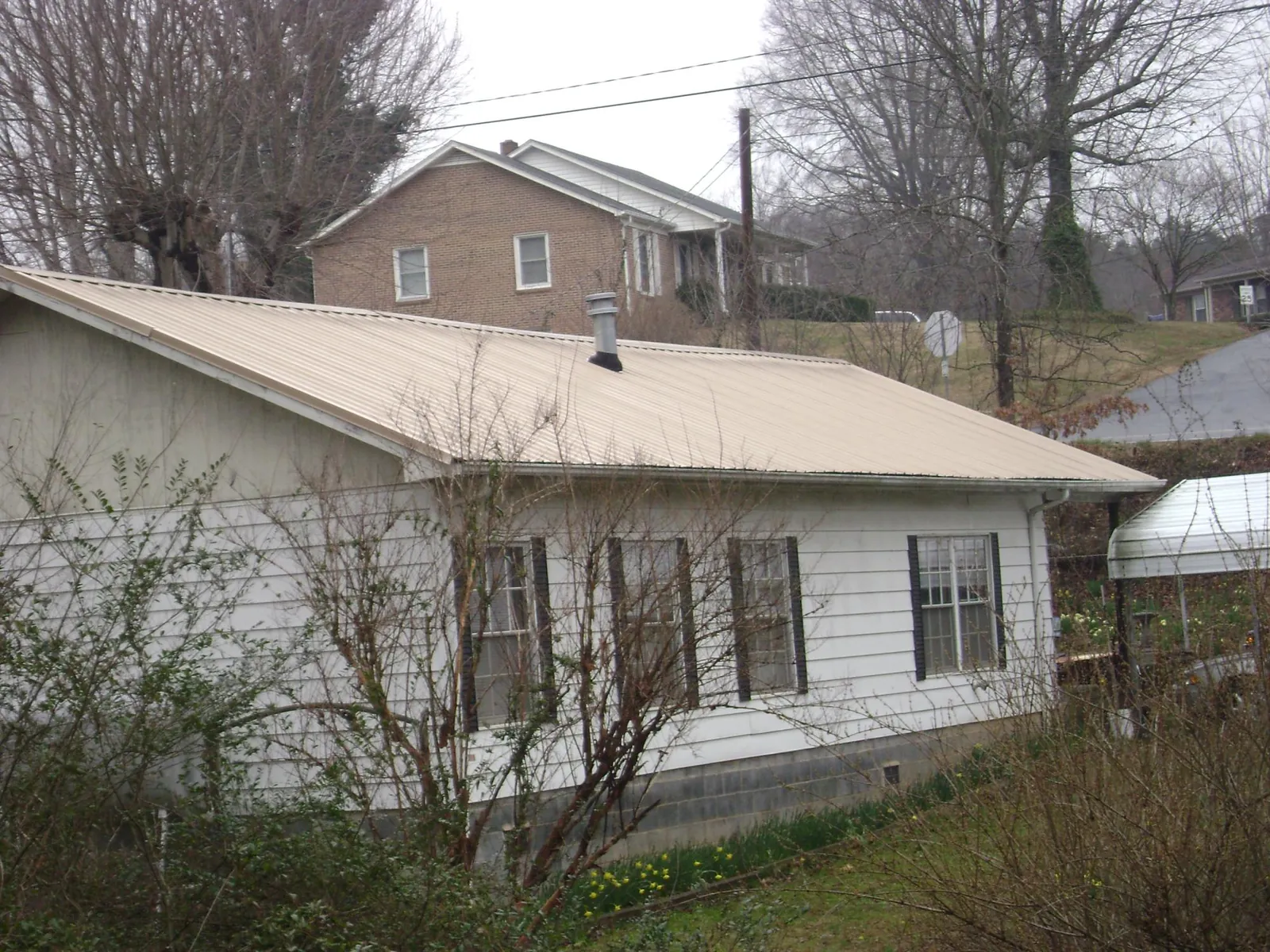 Tan metal roof on a white sided house set into a hillside — Commercial Roofing by Roofing Brothers in Manteno