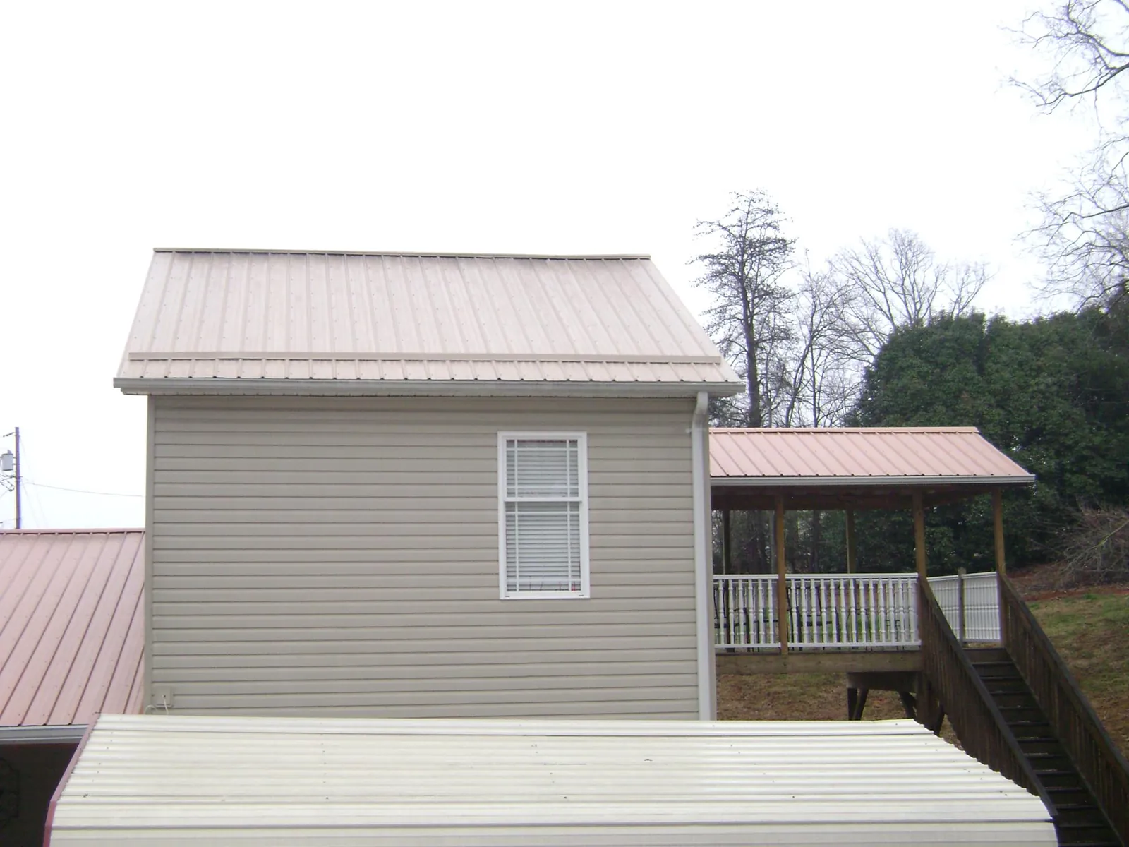 Tan metal roofs on a two story addition and attached porch, from a Roof Replacement job in Manteno
